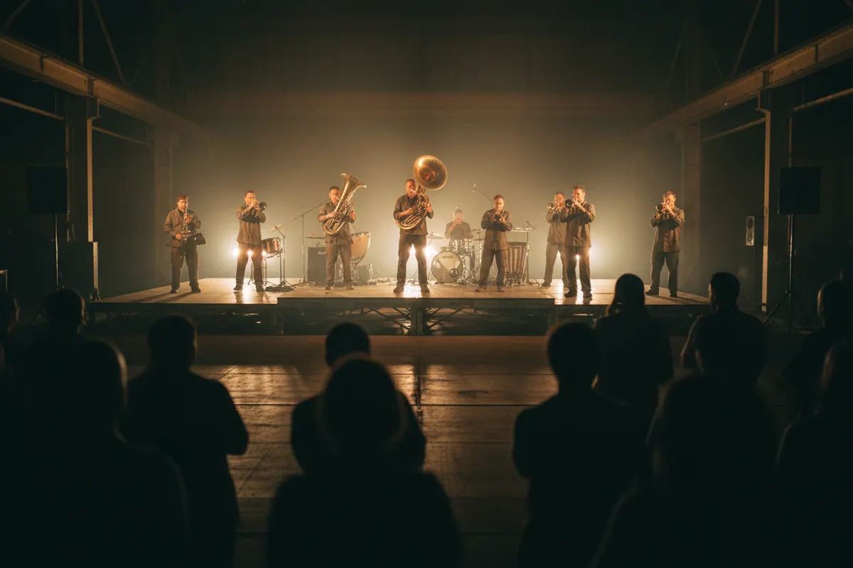A brass band playing on a low steel stage in a hazy factory hall